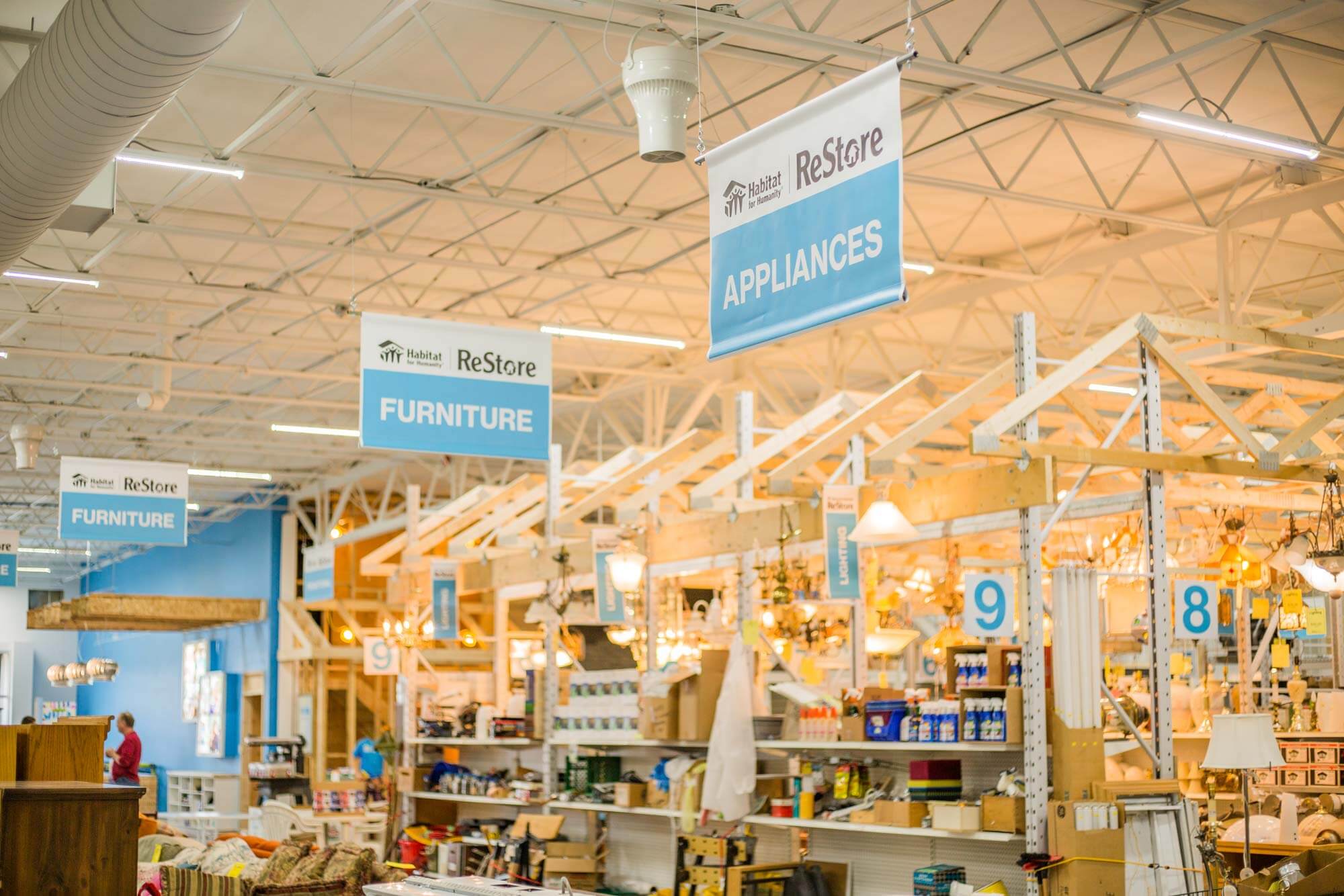 Photo of the interior of the ReStore ceiling showing the hanging aisle wayfinding banners, they read APPLIANCES, FURNITURE
