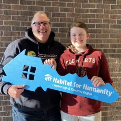 A father and his pre-teen daughter stand together beaming as they hold up an oversized Habitat branded house key cutout